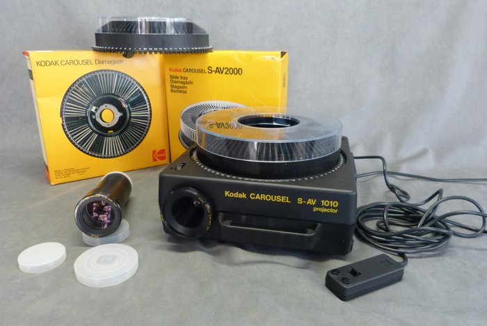 Kodak Carousel  Slide Projector  S- AV 1010  Met afstandsbedienings- kabel.  Halogeen lamp 24 V – lamp 250 watt. Hierbij 2 x carousel -Slide magazin. Verder   2 projectie lenzen ;  1 x Retinar S-Av 1000- 150 mm                                             