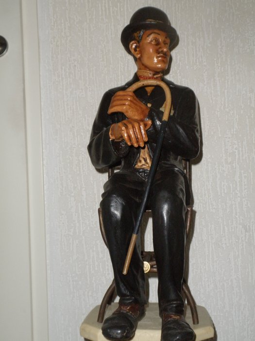 A very rare figurine of CHARLIE CHAPLIN sitting on a chair.