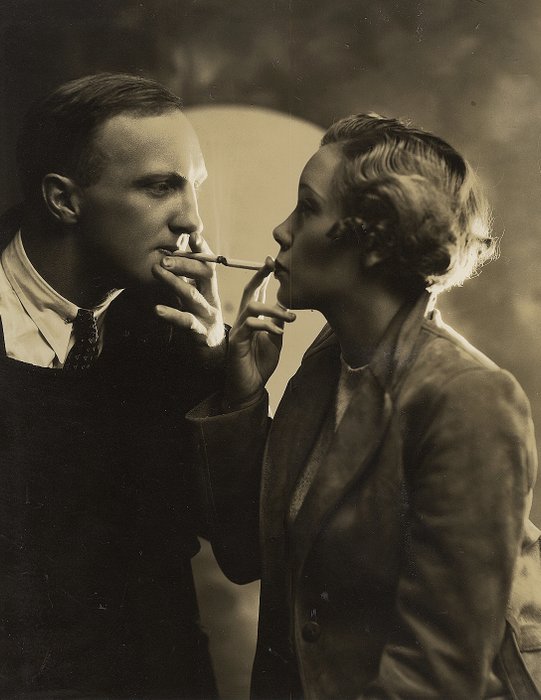 George Rinhart (XX)/Publishers Photo Service - Man Lights Woman's Cigarette With His Cigarette, c.1920s