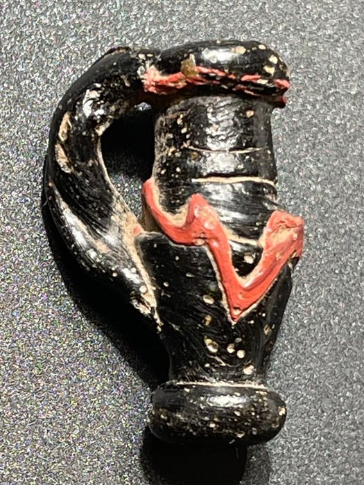 Oud-Romeins Ondoorzichtig Aantrekkelijk amulet in de vorm van een klassieke Oinochoe-vaas met een rond rood gekleurd ornament.
