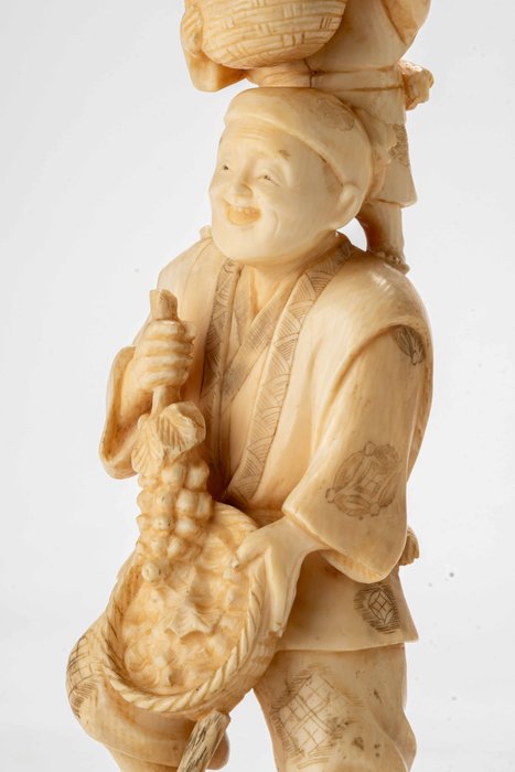 Marfim - Signed Shūgyoku 秀玉 - Um okimono de marfim representando um vendedor de frutas segurando uma cesta de uvas com uma criança - Período Meiji (final do século 19)