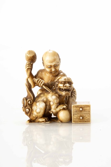 Marfim - Signed Rakumin 楽眠 - Um excelente okimono de marfim representando um artesão empenhado no ato de esculpir um shishi - Período Meiji (final do século 19)